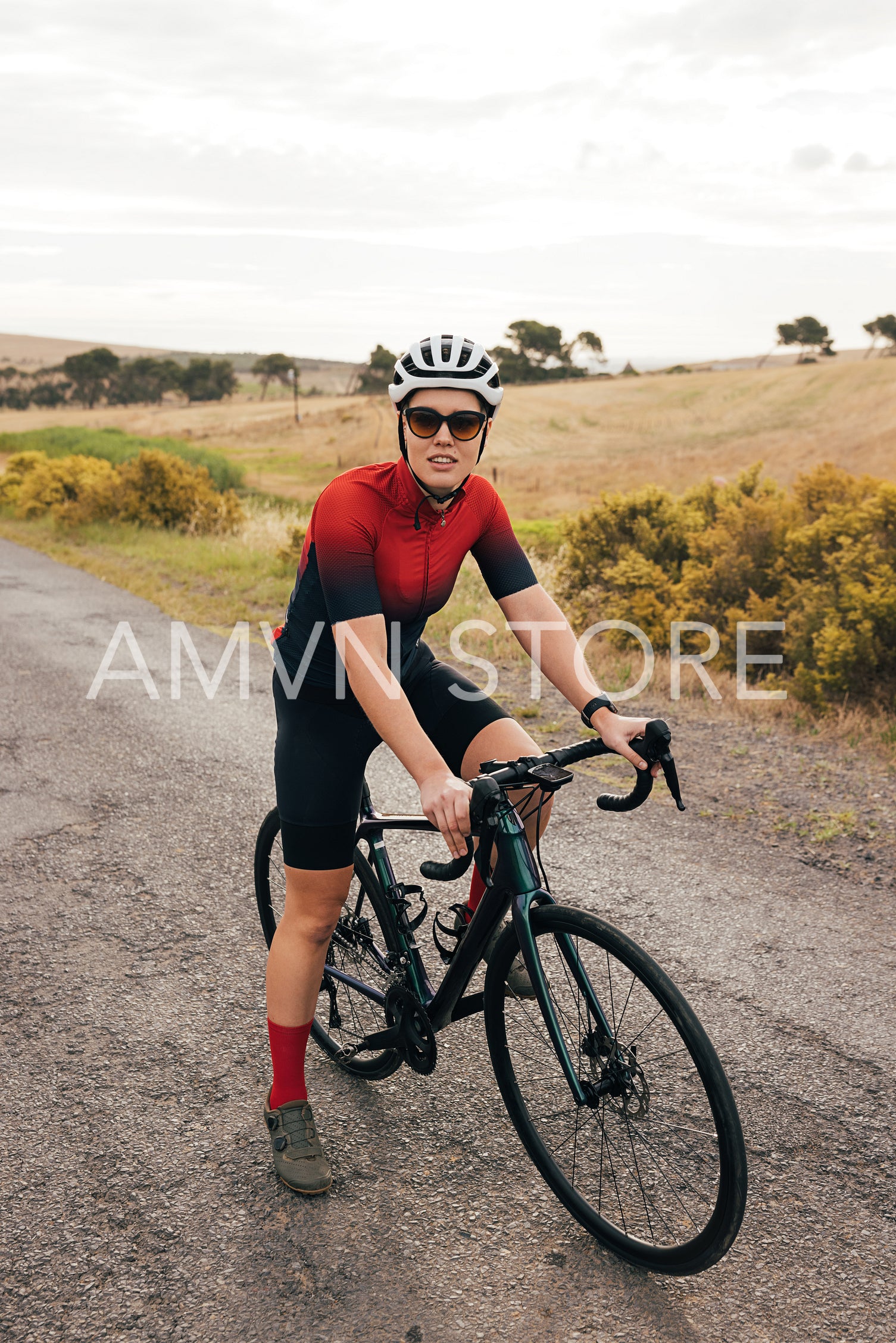 Female cyclist with a road bike standing on country road and looking at camera. Sportswoman with bicycle taking rest.