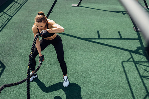 High angle view of fitness woman exercising with two battle ropes on a roof terrace