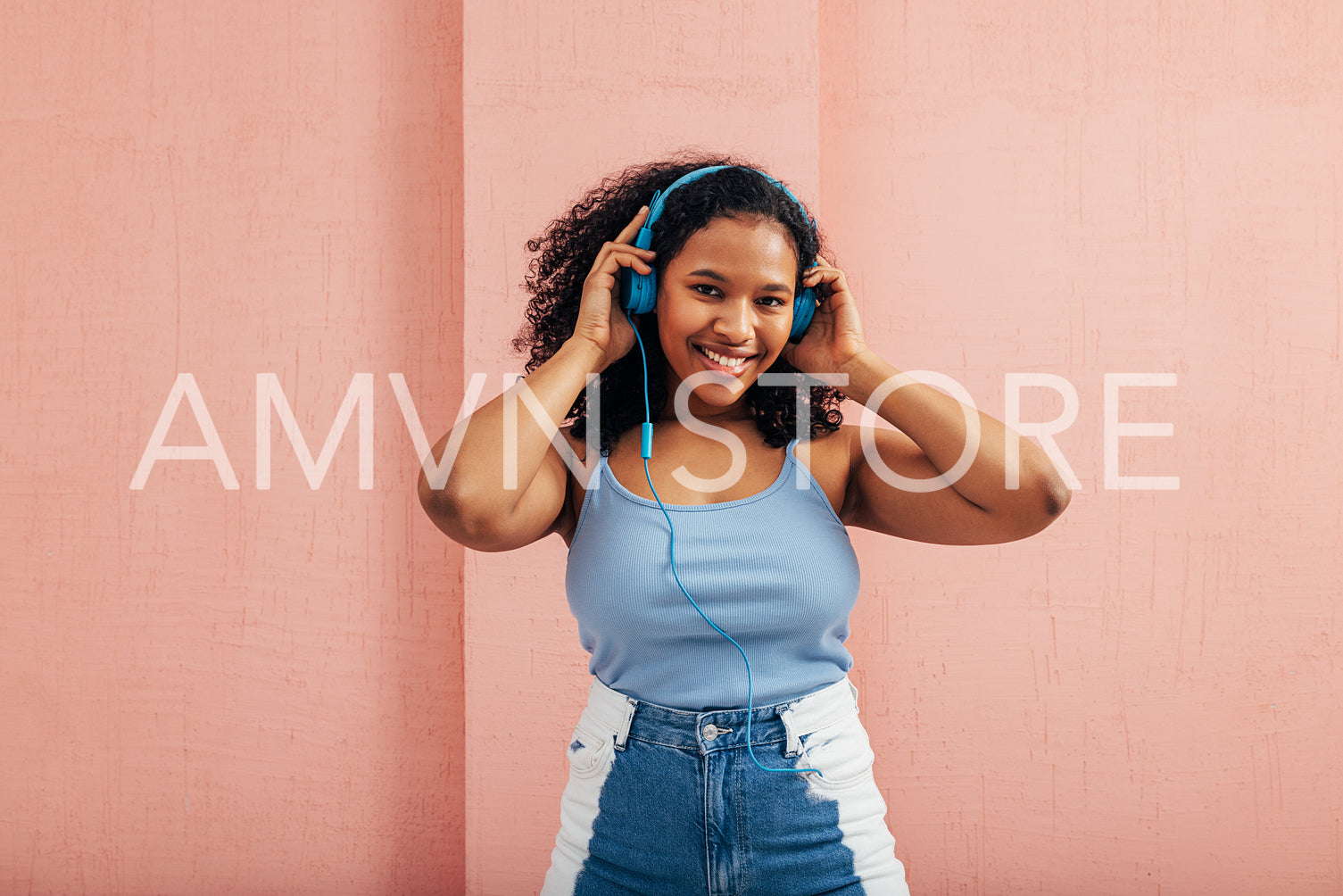 Smiling woman in casual clothes wearing blue headphones and looking at camera