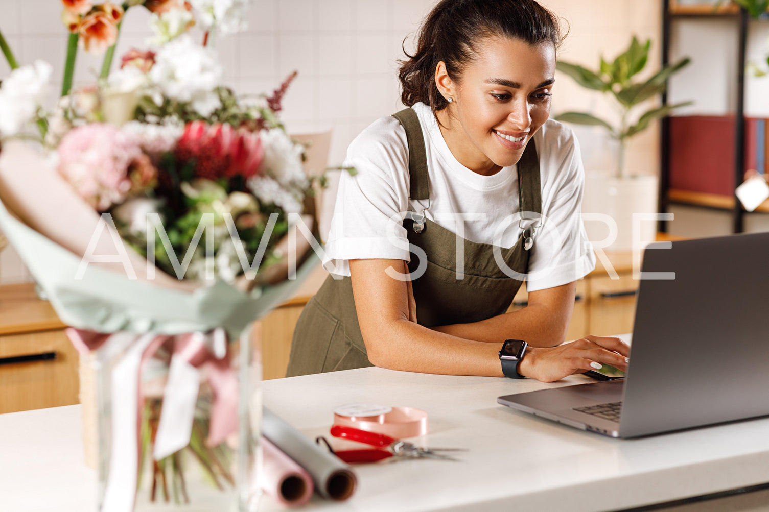 Smiling woman checking new orders on a laptop in her small flower shop	