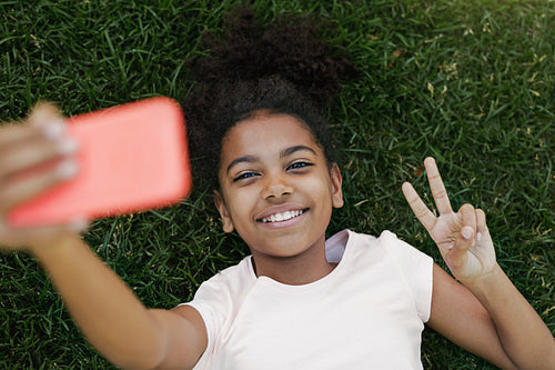 Smiling girl taking selfie on her smartphone, lying on grass in park