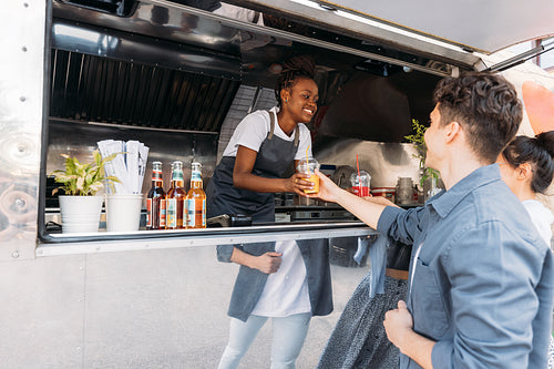 Smiling male and female customers receiving drinks from saleswoman. Young entrepreneur working in her a food truck.