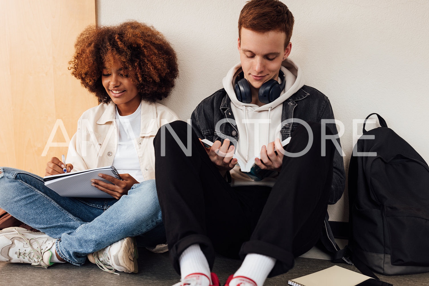 Two classmates sitting at wall in school. Students preparing their assignment while sitting together.