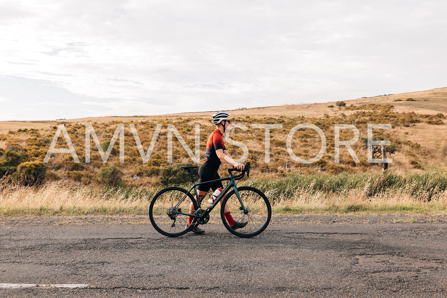 Side view of young professional cyclist walking with her road bike on countryside