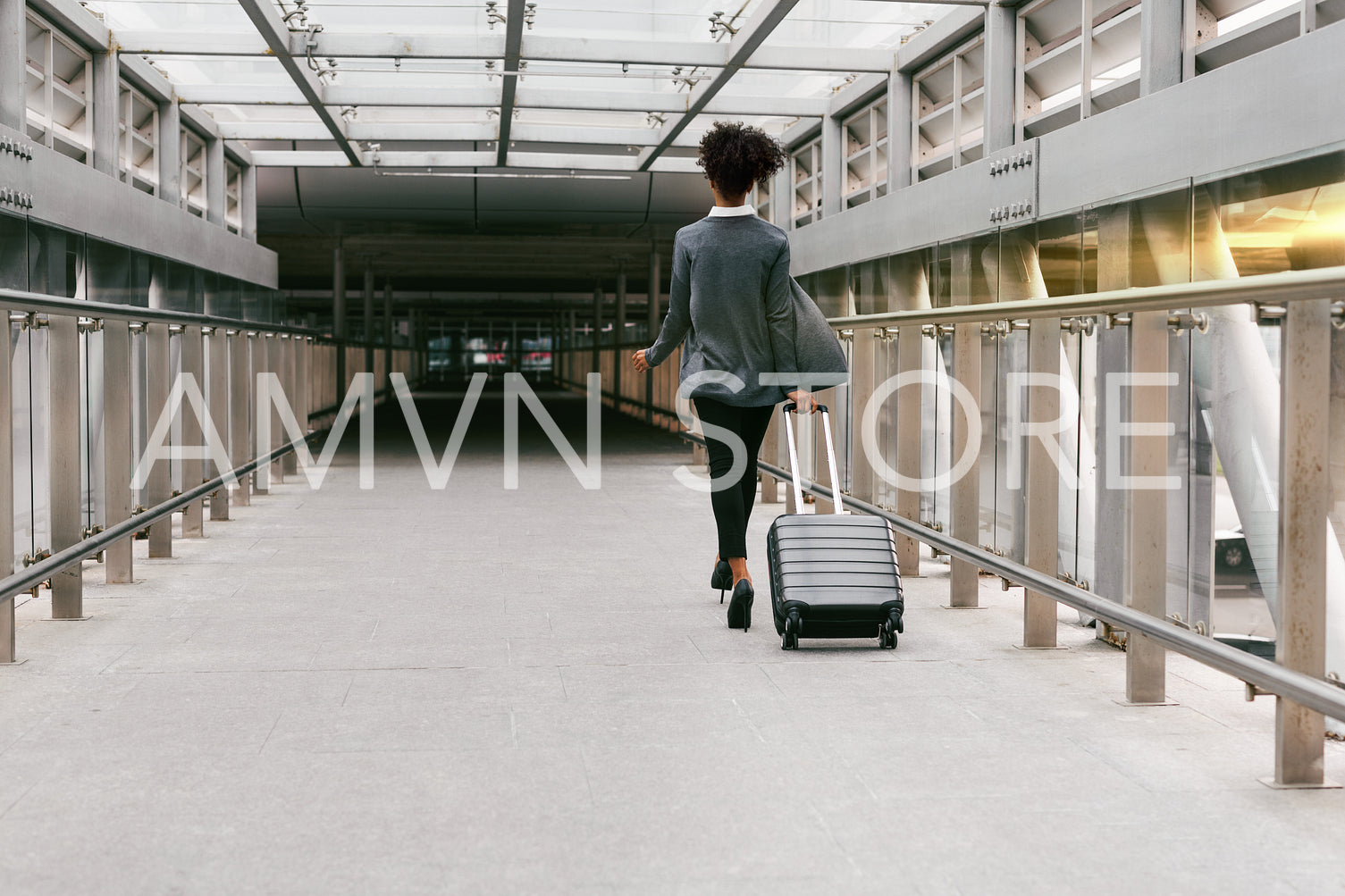 Businesswoman walking with suitcase in corridor, back view	