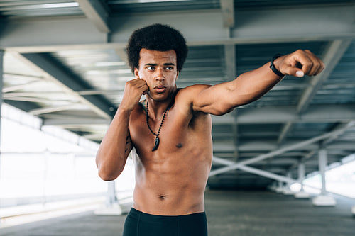 Male practicing boxing under a bridge, throwing a punch in front