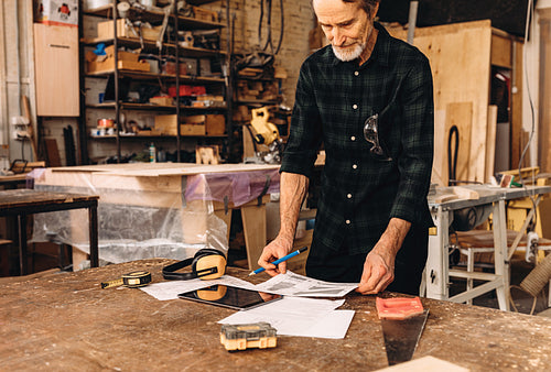 Male carpenter standing at workbench and reading document