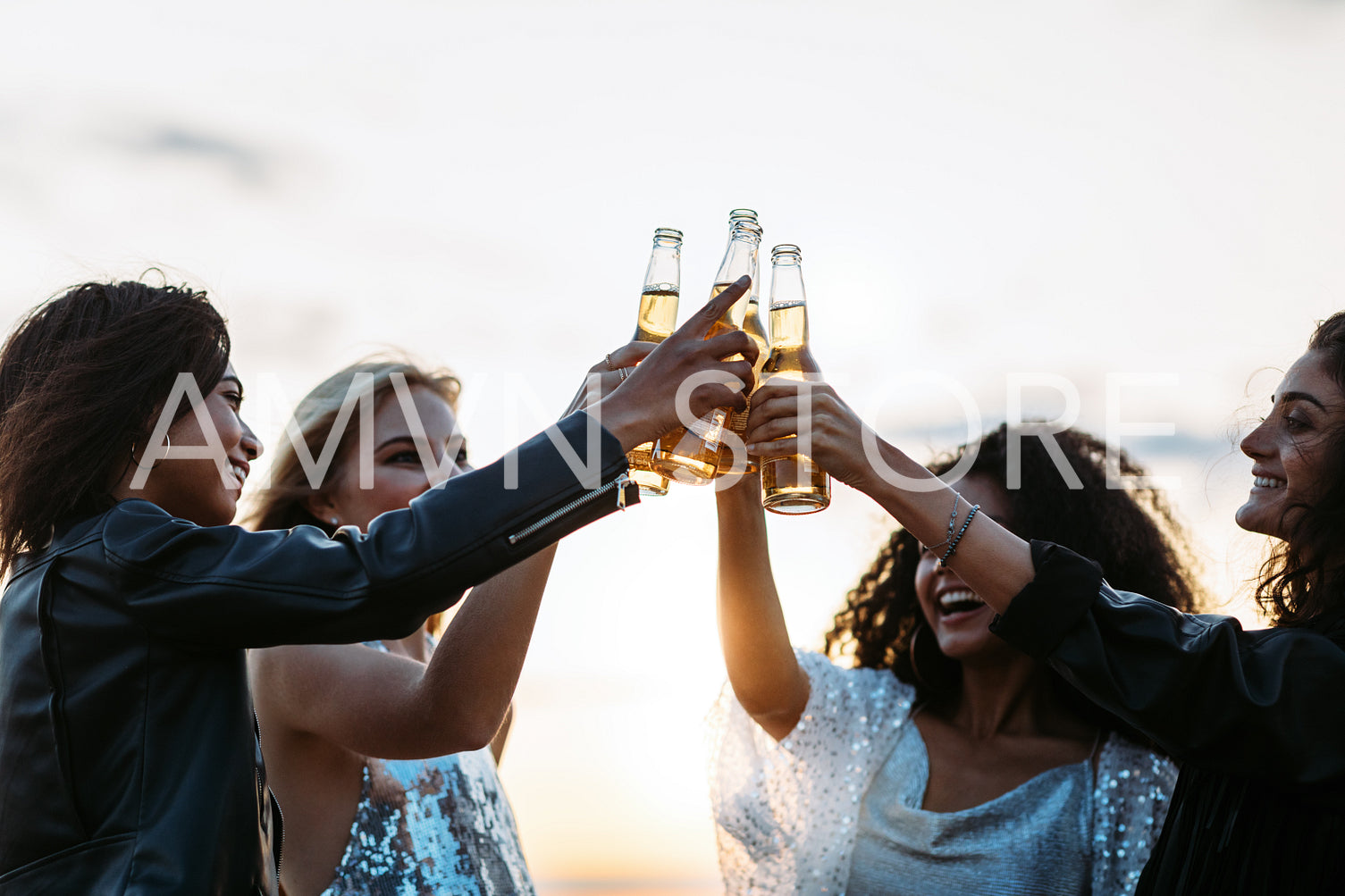 Multi-ethnic friends toasting beers at sunset. Women celebrating with beers in the evening.	