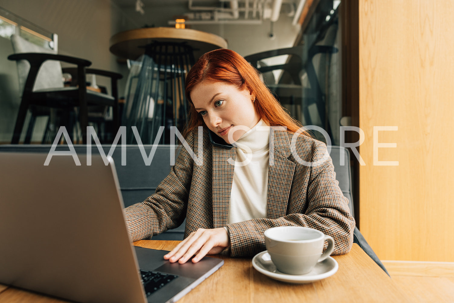 Woman working as a freelancer in a cafe. Female in formal wear typing on laptop and talk on a mobile phone.