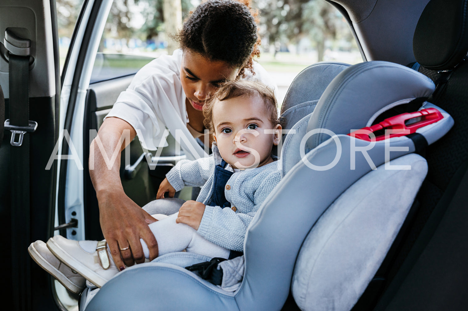 Little girl looking at camera while mother fasten belts on baby car seat	