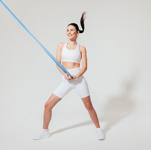 Full length of a slim woman in white fitness wear practicing with a resistance band in a studio