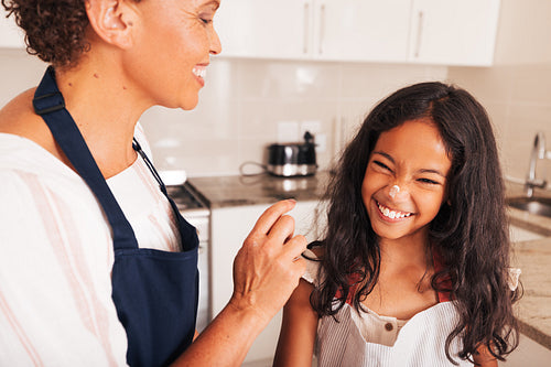 Smiling girl with flour on her nose. Grandma touching her granddaughter's nose with flour covered finger.