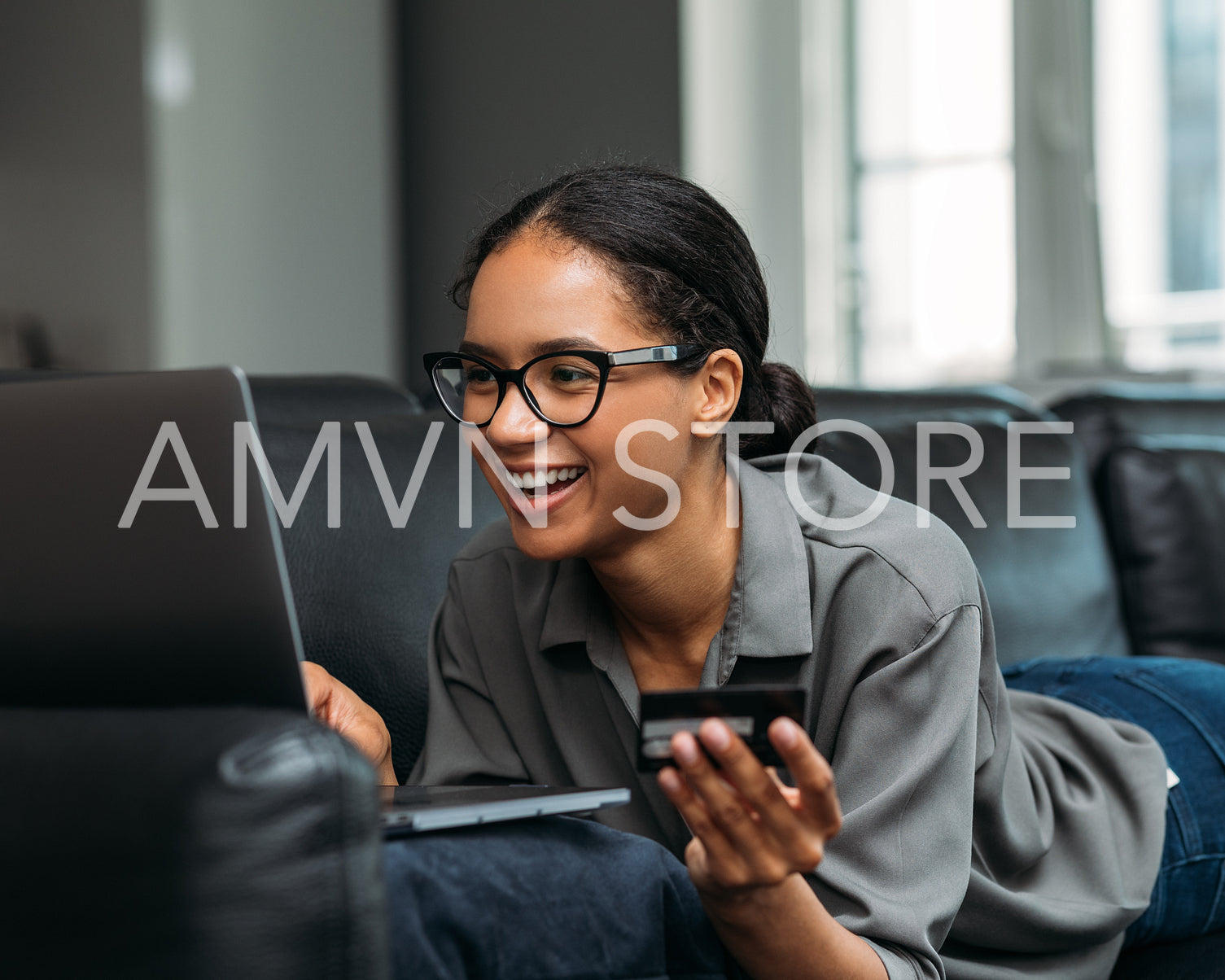 Happy woman making payment online while lying on a couch at home