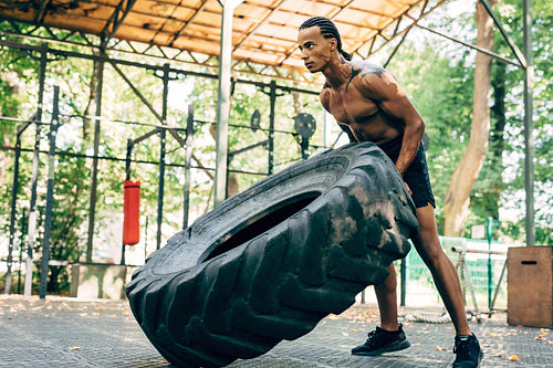 Muscular man exercising with heavy tire on sports ground outdoors