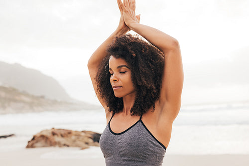 Cropped shot of a young woman with folded hands above her head meditating outdoors on a beach