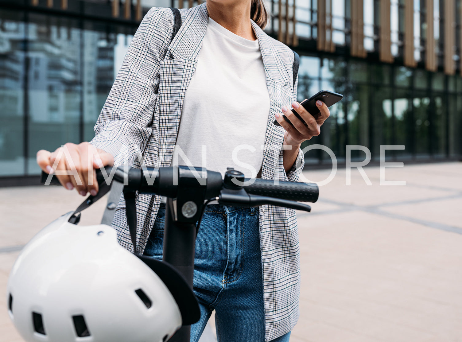 Unrecognizable businesswoman standing in front of an office building with electrical scooter and holding a smartphone 