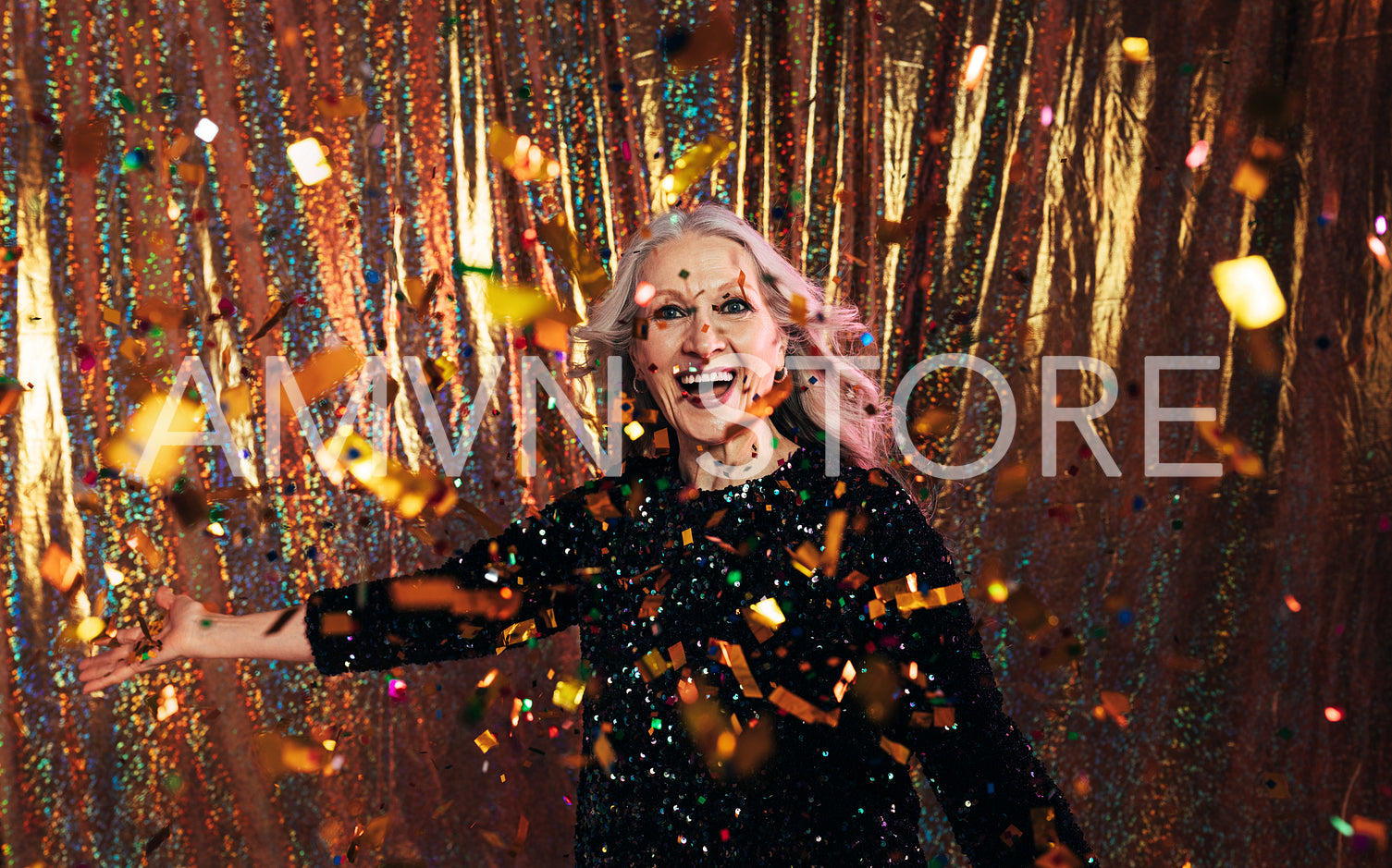 Stylish senior woman in black dress throwing confetti against a 