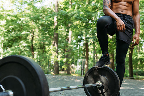 Cropped shot of a young muscular man standing outdoors after training. Unrecognizable athlete resting during exercises standing at the barbell.