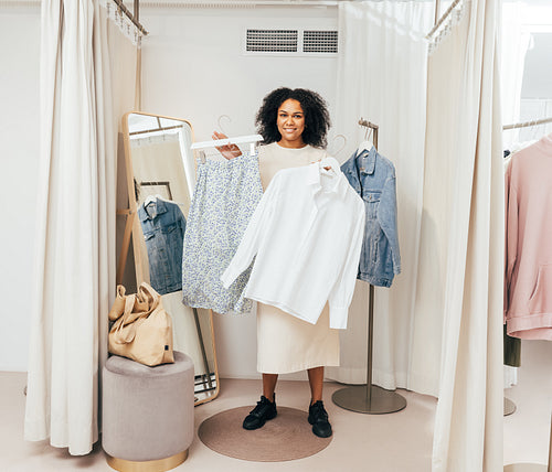 Stylish woman in fitting room standing with hangers looking at camera