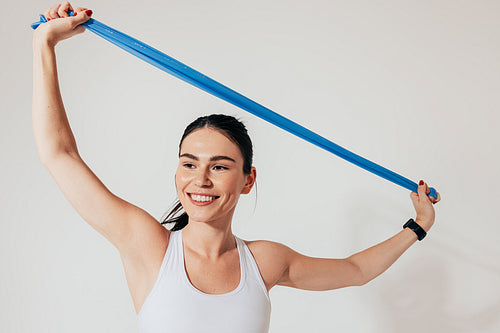 Young smiling woman with resistance band stretching her hands against the white backdrop