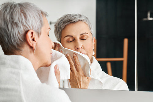 Mature woman with short grey hair using a towel after washing up face