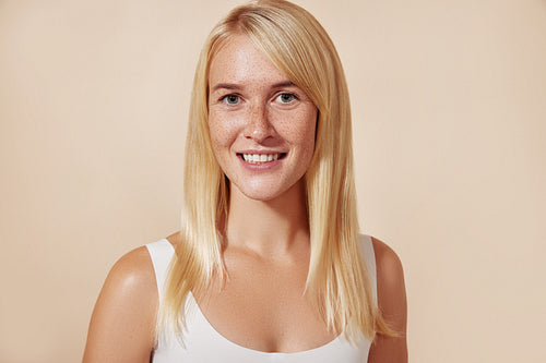 Portrait of a beautiful woman with freckles in studio. Young female with perfect skin against a beige backdrop.