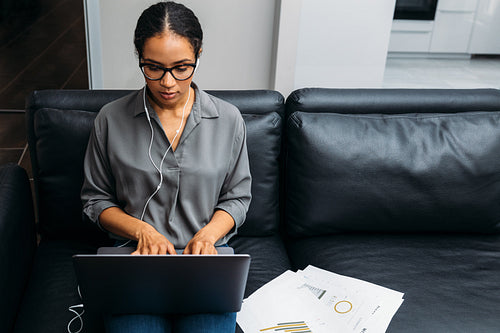 Front view of a young woman working online with documents while sitting on sofa