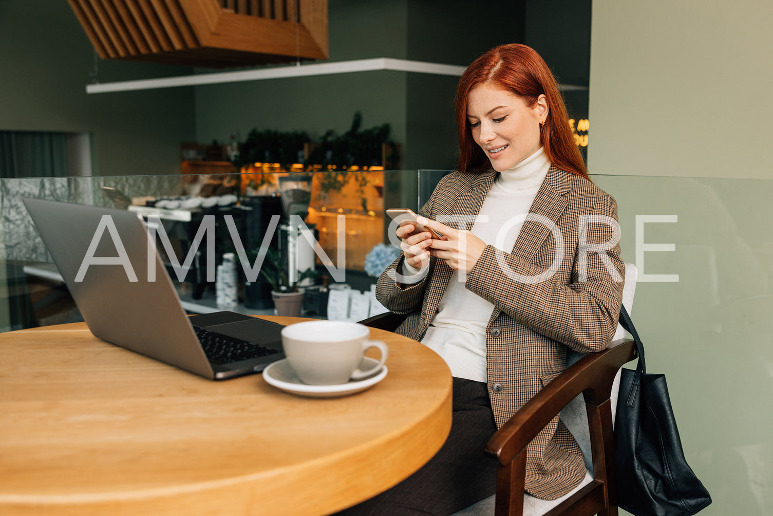 Smiling businesswoman with a smartphone in cafe. Female with ginger hair in formal wear sitting at a table.