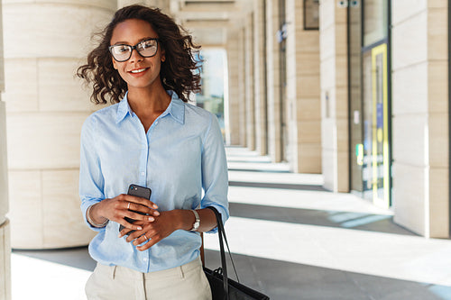 Smiling woman holding a cell phone with office building on background