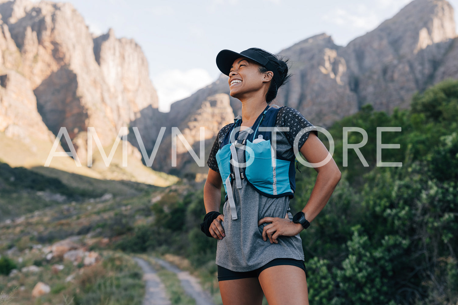 Laughing woman in sportswear standing against mountains. Young smiling female relaxing during hike.