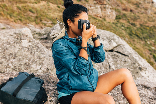 Woman tourist taking photographs on a film camera sitting on a rock