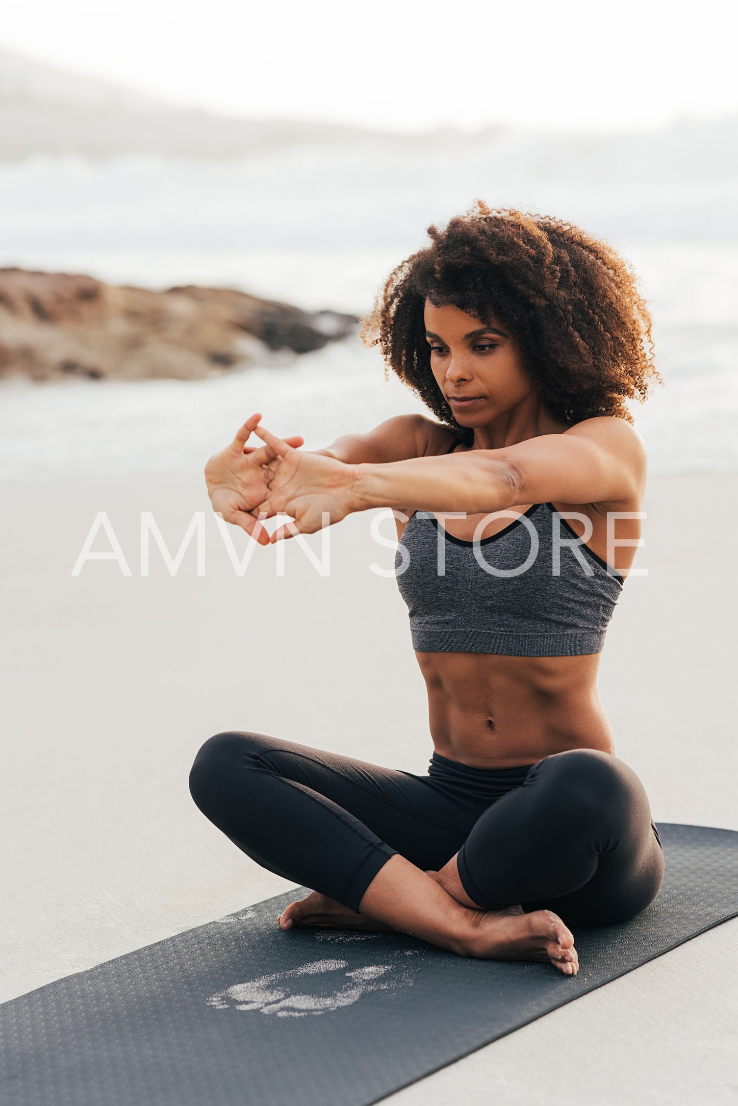 Young woman sitting on mat on a beach warming up her hands 