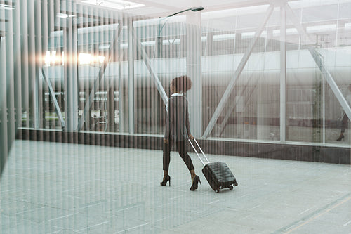 Modern businesswoman pulling her suitcase, back view shot through window