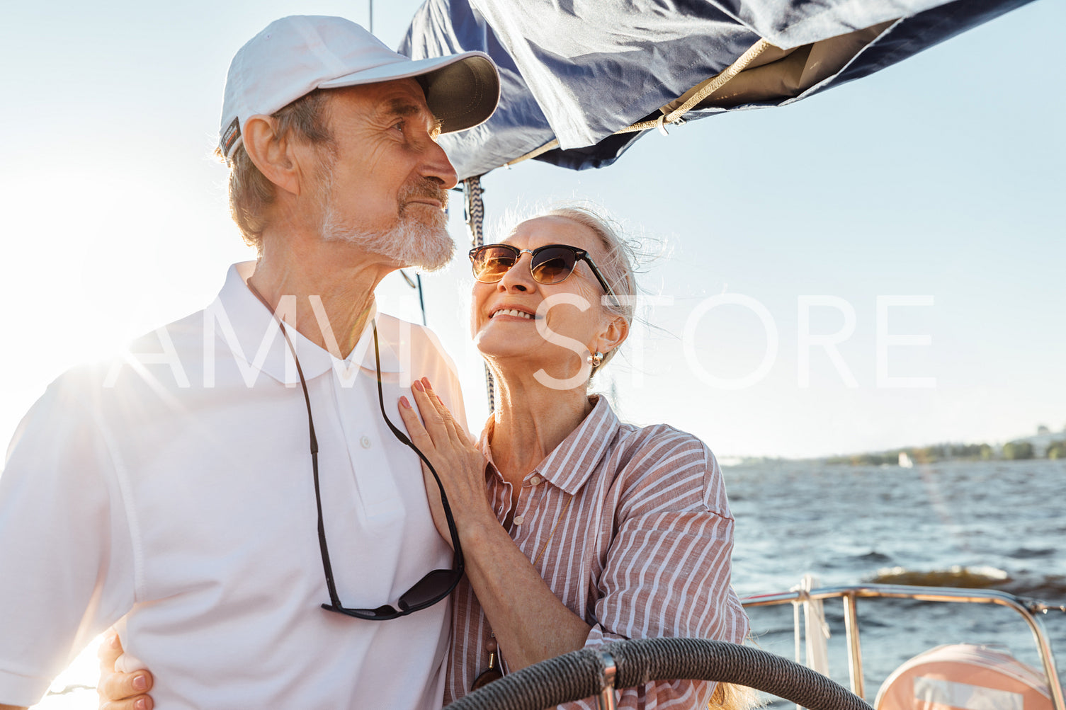 Happy mature woman looking on her husband while he steering a yacht. Affectionate couple enjoying a vacation on private sailboat at sunny day.	