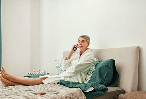 Mature woman talking by phone lying on her bed after home spa