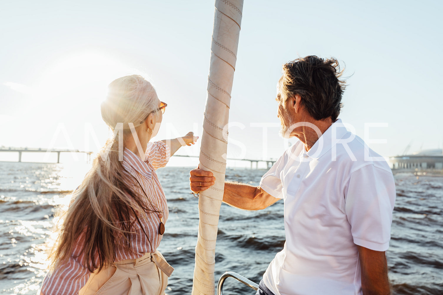 Rearview of two mature people sitting on a sailboat bow and enjoying summer day	