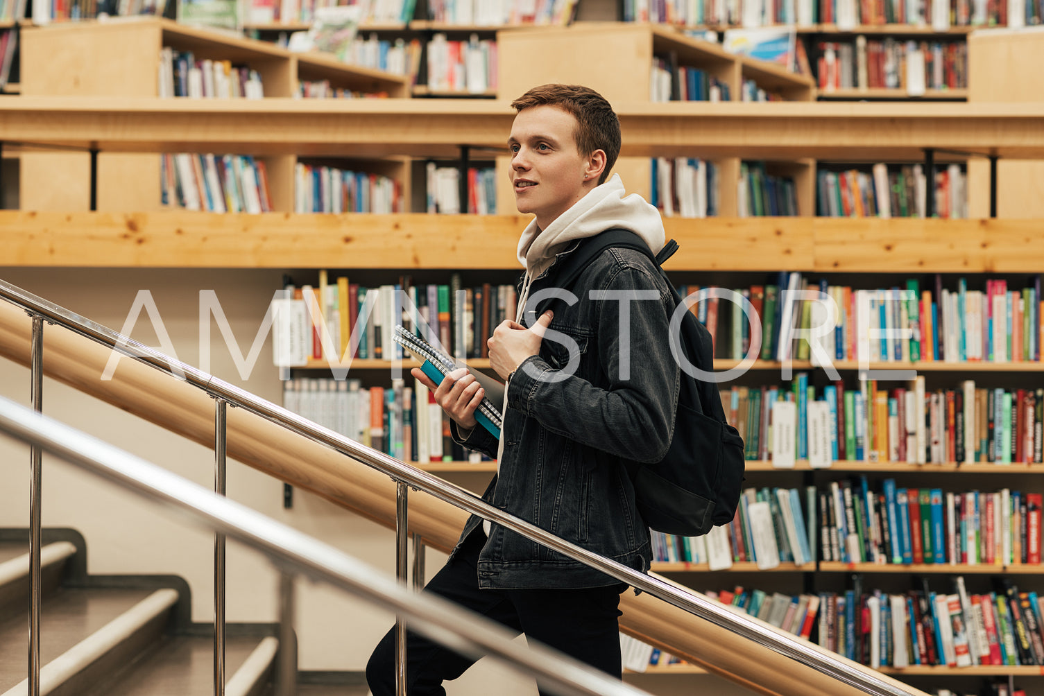 Young male student going up the stairs in library. Man with textbooks in university library.