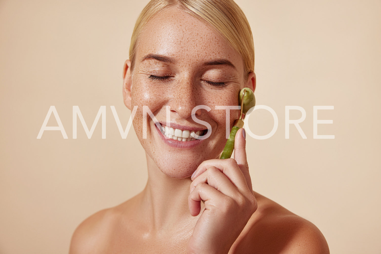 Happy woman with freckles and smooth skin using a jade stone roller