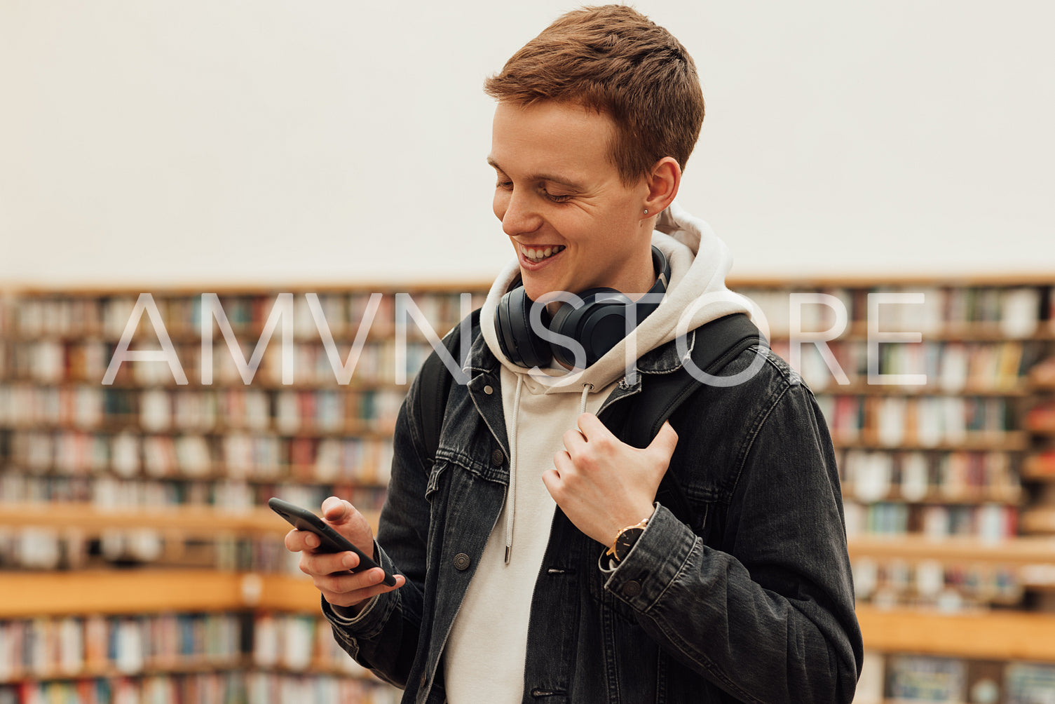 Smiling student using smartphone while standing in library