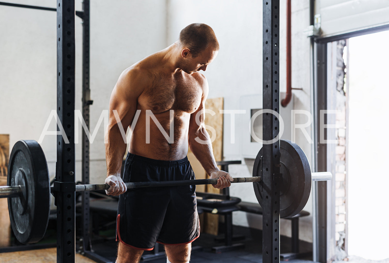 A muscular young man working out with barbell in sport club