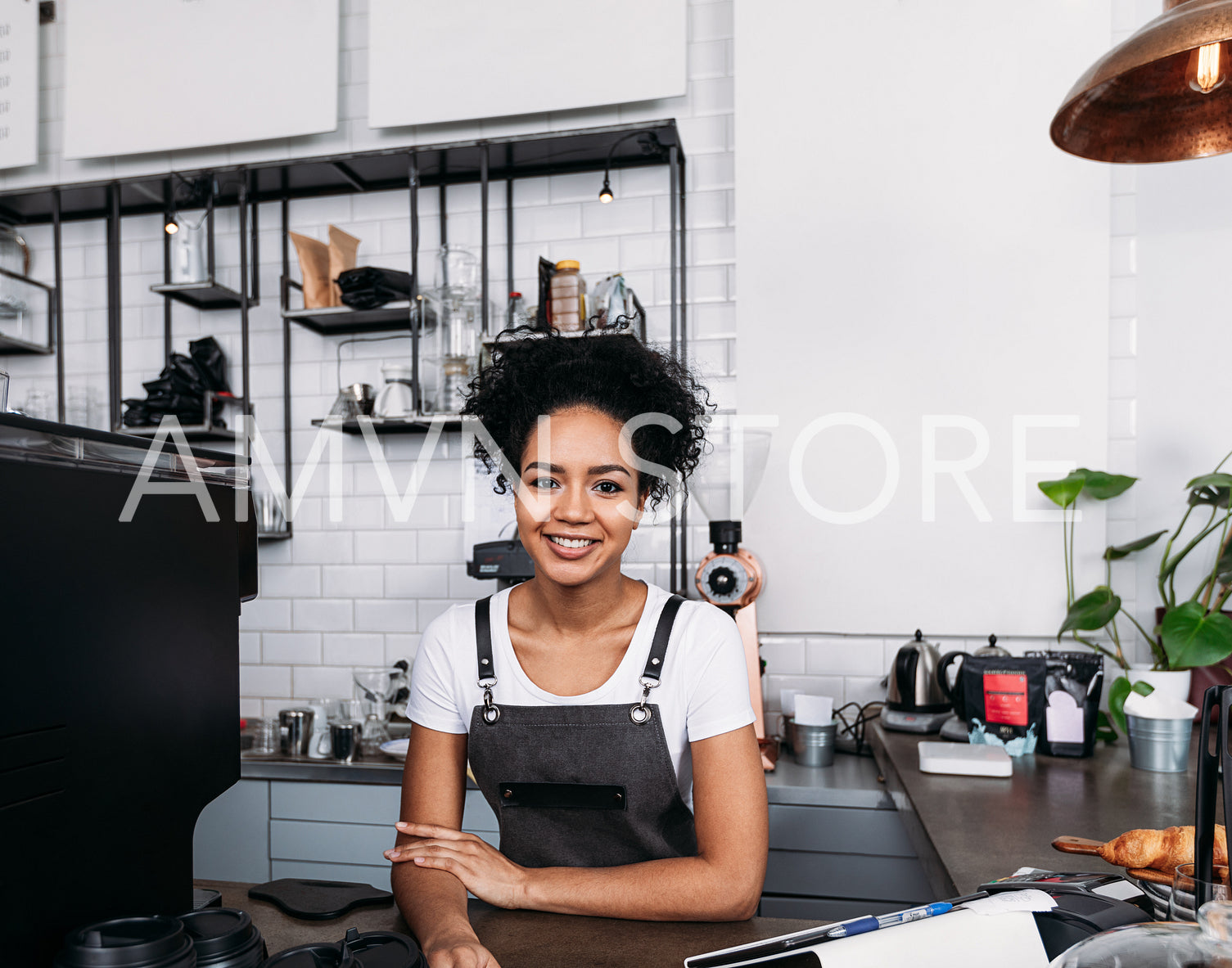 Waitress with curly hair in an apron standing at a counter in a cafe and looking at camera