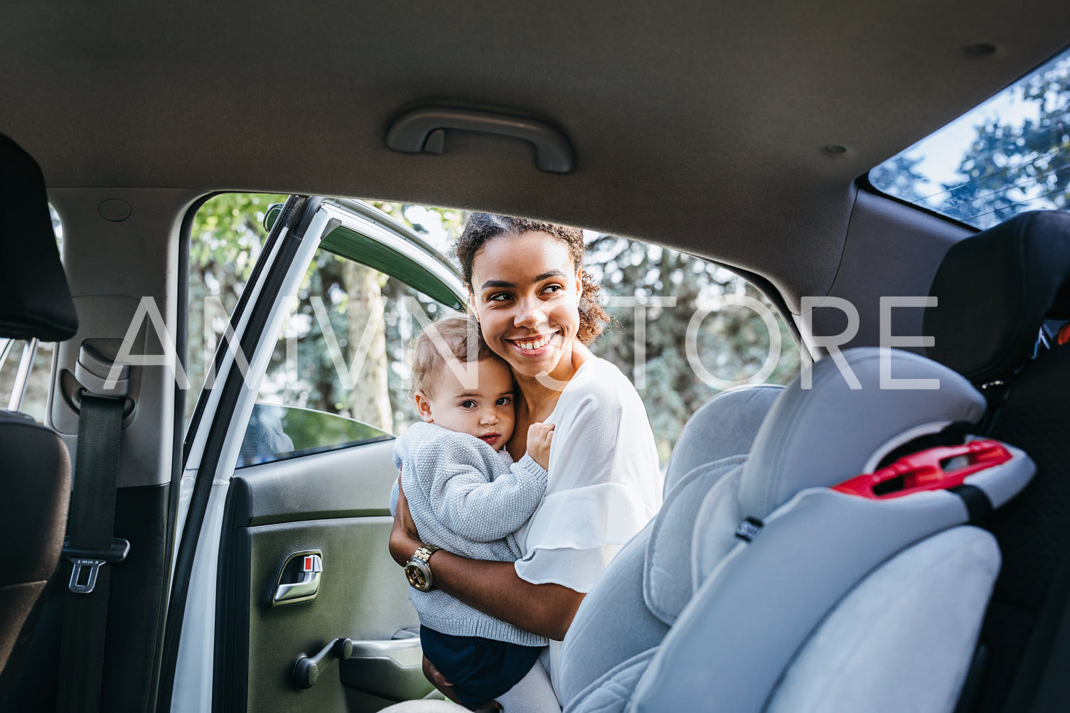 Smiling mother putting baby daughter in a car seat. Young woman holding a child on hands near a car.	