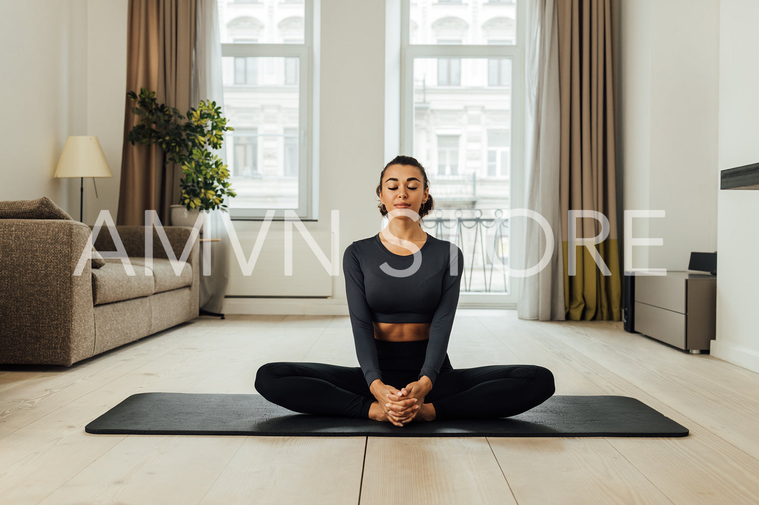 Young woman in sports clothes meditating on a mat in living room	