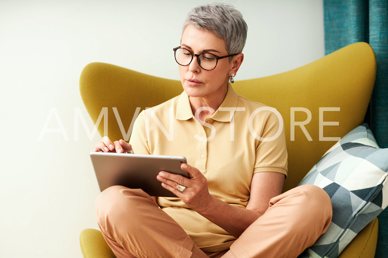 Mature woman sitting with crossed legs on armchair using a digital tablet	