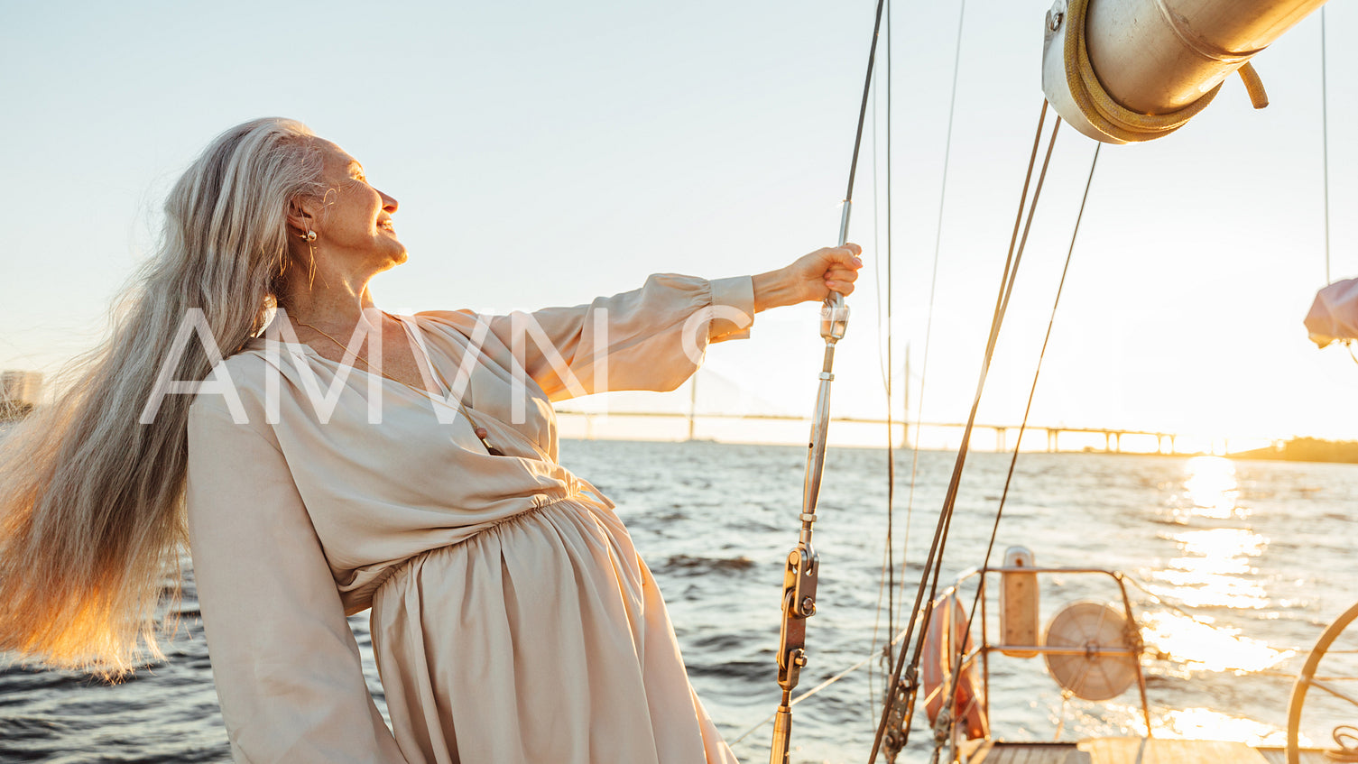 Elderly woman with long hair holding a rope and enjoying sunset on sailboat	