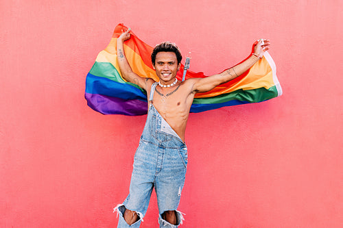 Happy guy waving rainbow lgbt flag against pink wall outdoors