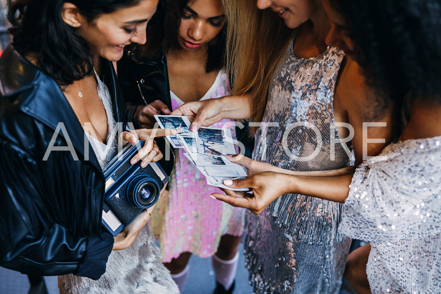 Young female friends standing with instant camera and photographs they made during party outdoors	