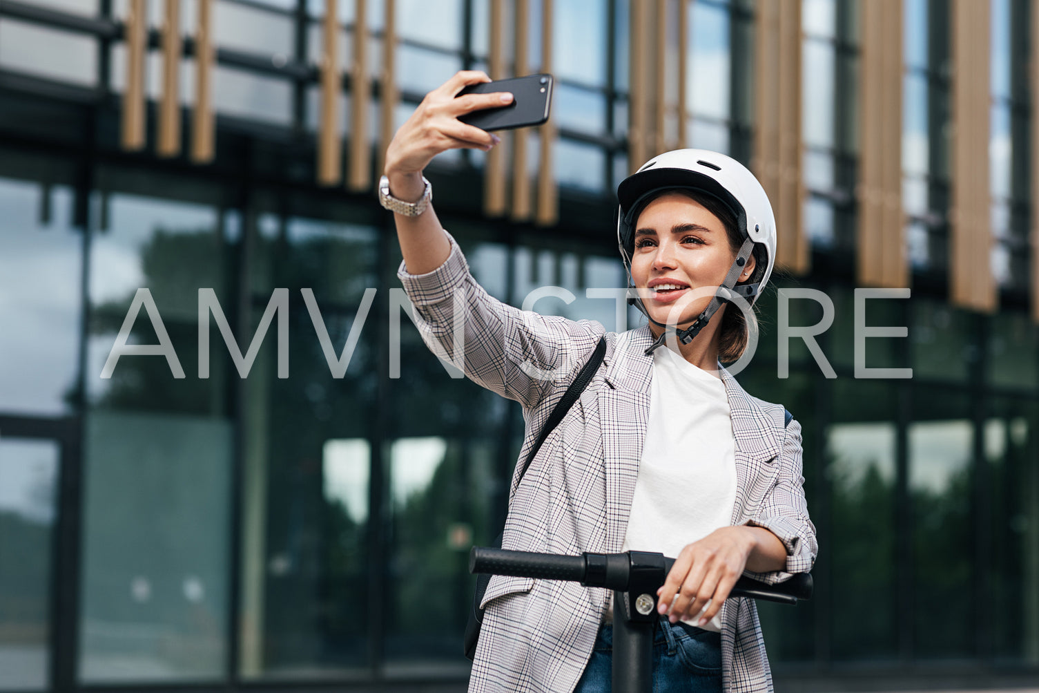 Young beautiful woman in a white cycling helmet taking selfie while standing on an electric push scooter in the city