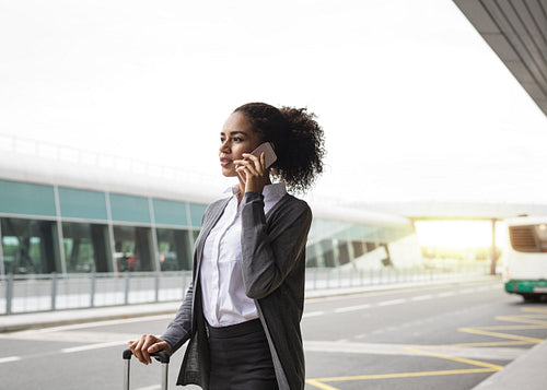 Young woman talking on mobile phone at airport terminal, waiting for a taxi