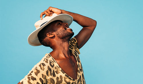 Happy stylish man hiding his face with white straw hat against blue background